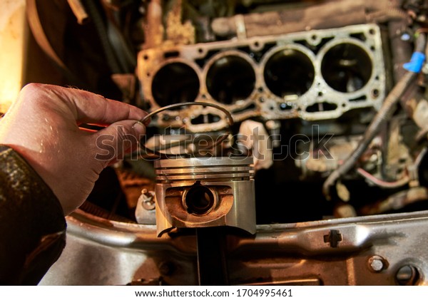 A man holds a piston of a car against\
the background of an engine, car repair\
process.