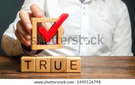 A man holds a red check mark over word True. Confirm the veracity and truth. Fight against fake news hostile propaganda. Confirmation facts, refutation of rumors. Debunking Myths and Misconceptions