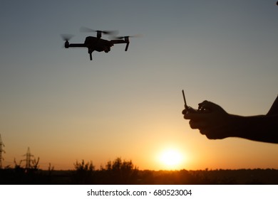 Man holds remote controller with his hands while copter is flying on background. Drone hovers behind the pilot on suset.