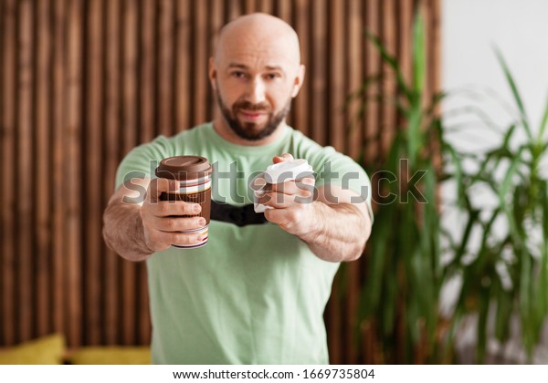The man holds a reusable Cup in one\
hand and a plastic Cup in the other. Against the use of disposable\
plastic. The right choice, the environmental\
choice