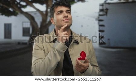 Man holds ring while holding out on street by young hispanic guy expecting romantic proposal and shows thoughtful expression.