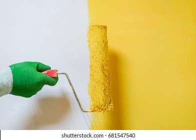 Man Holds Roller Brush With Yellow Paint Over Yellow Half Painted Wall