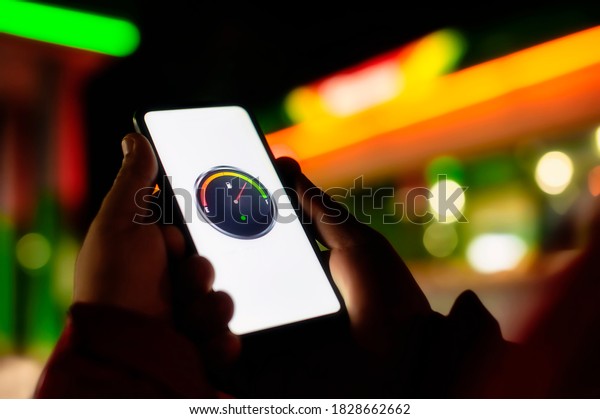 A
man holds a smartphone with a digital fuel meter on the screen
against the background of a night gas station for a
car