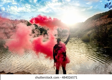 Man Holds Up Smoke Flare To Signal For Help In The Middle Of Nature. Lake On Mountain