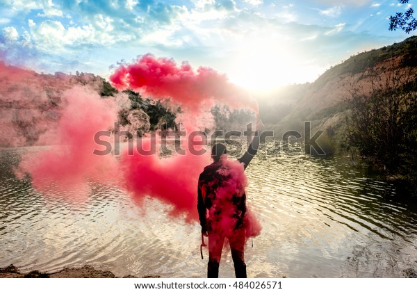 Man holds up smoke flare to signal for\
help in the middle of nature. Lake on\
mountain