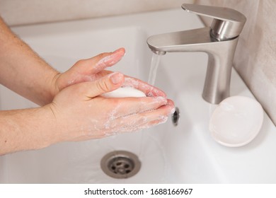 A man holds soap in his hands over the washbasin. Closeup of hands with soap. Hand disinfection during a coronavirus pandemic. Life-saving hygiene procedures. - Shutterstock ID 1688166967