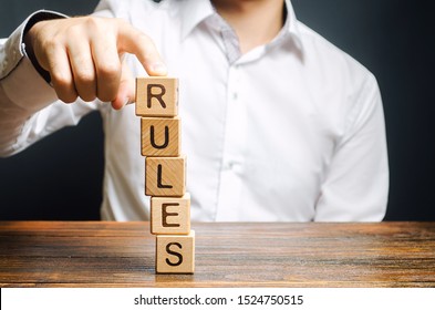 A Man Holds A Tower Of Blocks With The Word Rules From Falling. Setting Clear Rule And Restrictions. Leadership And Discipline. Authoritarianism, Tight Control Framework. Norms And Laws In Society