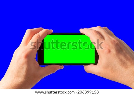 Man holds in two hands tablet PC in landscape mode with green screen isolated on blue. Chroma key screen for placement of your own content. 