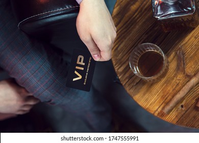 Man holds VIP member card in his hand. View from the top on the gentleman's hand that holds exclusive VIP membership card next to the wooden table with whisky in carafe and glass with cigar.