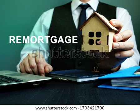 Man holds wooden home and sign remortgage.