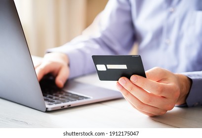 A Man From Home Buys Goods In An Online Store In The Context Of A Coronavirus - A Close-up Of A Laptop And A Credit Card In A Man's Hand - Purchase Of Goods At A Distance With Modern Technologies