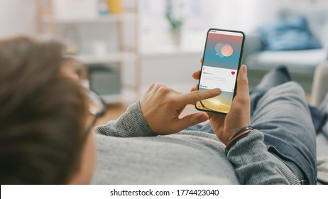 Man At Home Lying On A Couch Using Smartphone, Scrolling Social Media Feed, Checking News, Friends Activity. Guy Using Mobile Phone, Internet Social Networks Browsing.