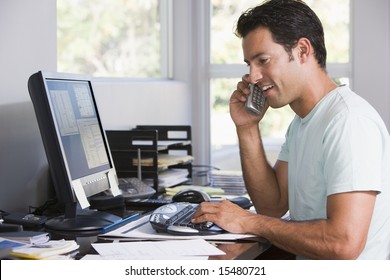 Man in home office on telephone using computer and smiling