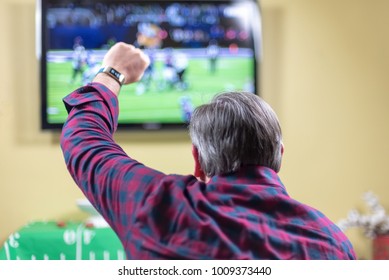 Man At Home Sitting On Couch Cheering At Football Game On TV Screen