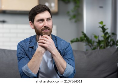 The man at home is sitting on the couch, resting looking away, smiling dreamy pensive - Shutterstock ID 2137364511