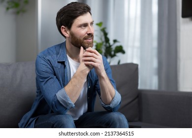 The man at home is sitting on the couch, resting looking away, smiling dreamy pensive - Shutterstock ID 2137364515