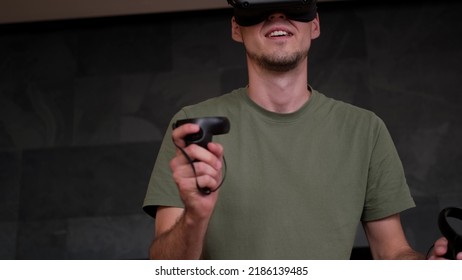 Man At Home Wearing Virtual Reality Headset Holding Gaming Controllers. Active VR Game Virtual Reality Technology Gaming Simulation Helmets. Metaverse Oculus Technology