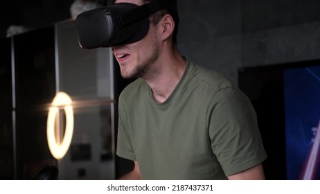 Man At Home Wearing Virtual Reality Headset Holding Gaming Controllers. Active VR Game Virtual Reality Technology Gaming Simulation Helmets. Metaverse Oculus Technology