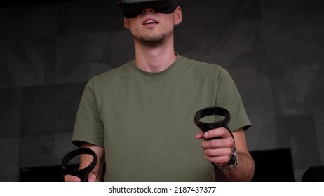 Man At Home Wearing Virtual Reality Headset Holding Gaming Controllers. Active VR Game Virtual Reality Technology Gaming Simulation Helmets. Metaverse Oculus Technology