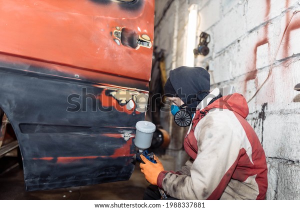 man in a home workshop paints a truck red with a\
spray bottle
