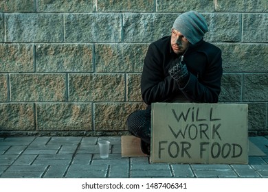 A Man, Homeless, A Man Asks For Alms On The Street With A Sign Will Work For Food. Concept Of Homeless Person, Addict, Poverty, Despair