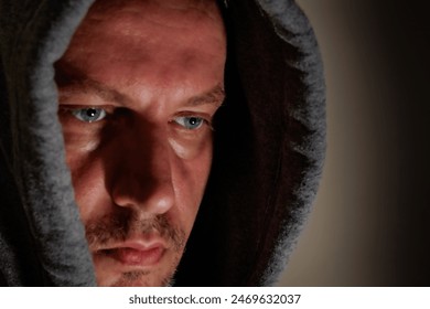 Man with a hood, intense blue eyes, detailed portrait, dark background, serious expression, dramatic lighting, mysterious look, face detail, introspective mood. - Powered by Shutterstock