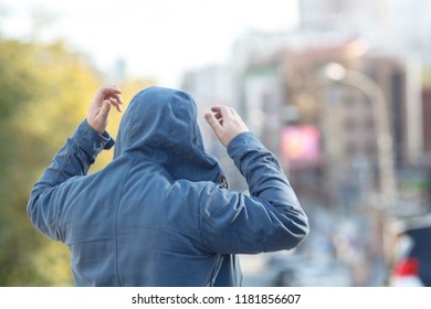 man in hood, looking away, cityscape behind him - Shutterstock ID 1181856607