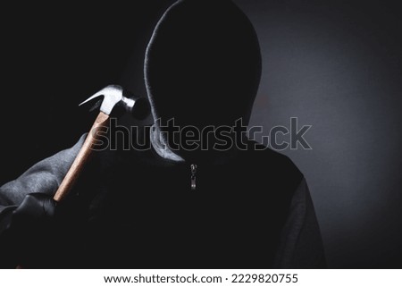 man with a hood and a mask on his face threatens with a hammer