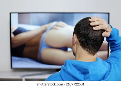 Man in hoodie looking at sensual woman on TV screen. Concept of internet web model, adult movie