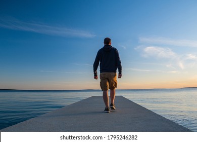 Man in hoodie and short cargo pants on dock, sea horizon in background, island od Pag, Adriatic sea, Croatia