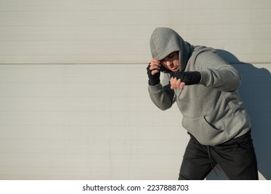 A man in a hoody trains boxing against a gray wall.  - Powered by Shutterstock