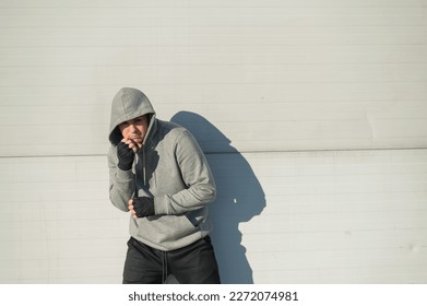 A man in a hoody trains boxing against a gray wall.  - Powered by Shutterstock