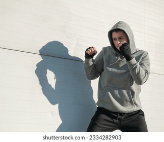 A man in a hoody trains boxing against a gray wall.  - Powered by Shutterstock