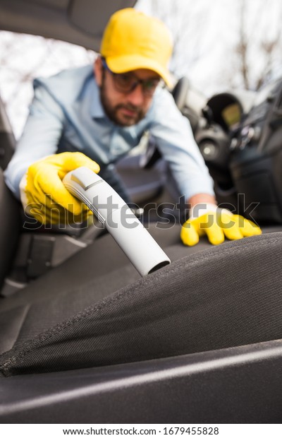 Man hoovering passenger seat, car wash and\
cleaning concept.
