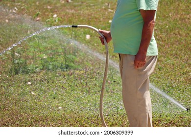 Man with a hose in his hand is watering the grass. Gardener takes care of the lawn in hot weather - Powered by Shutterstock