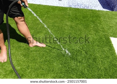 man hoses down artificial grass so it doesn't burn his feet