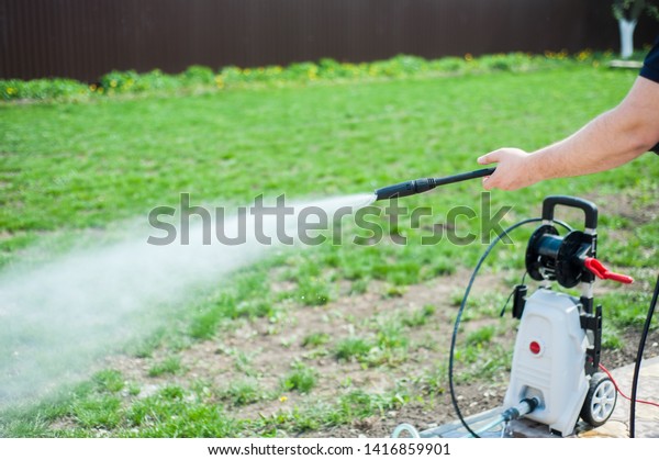 A man hoses a portable car for washing the car in\
nature. Space for text