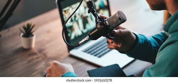 A man host streaming his audio podcast using microphone and laptop at his small broadcast studio, close-up - Shutterstock ID 1931610278