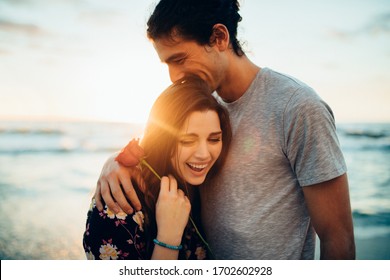 Man hugging his girlfriend holding a rose at the beach. Couple on their first date at the beach.