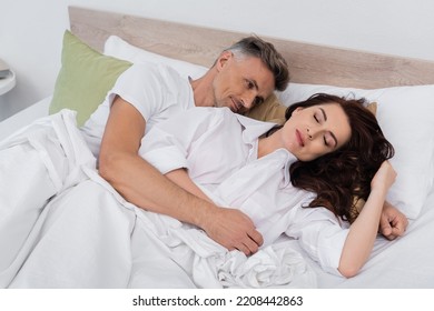 Man Hugging Sleeping Brunette Wife On Bed At Home