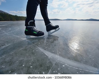 Man Ice Skating On Frozen Lake. Thin Ice With Deeep Cracks Below Man Legs.