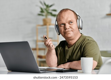 A man with inclusivity wearing headphones sits at his desk in his home office working. - Powered by Shutterstock