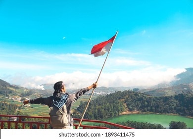 A Man With Indonesian Flag Standing On Cliff And Enjoying The View Of Nature Of Lake And Mountain In Dieng Indonesia.