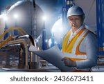 Man industrialist near manufactory. Plant technologist with construction documentation. Guy is factory engineer. Industrialist looks at camera. Man near evening factory. Industrialist in orange vest