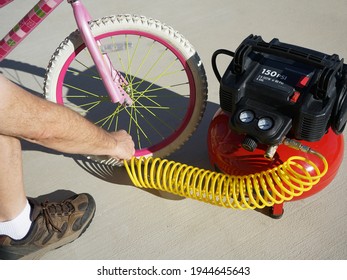 A man inflating childs bicycle tire with air from compressor.