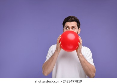 Man inflating red balloon on purple background. Space for text