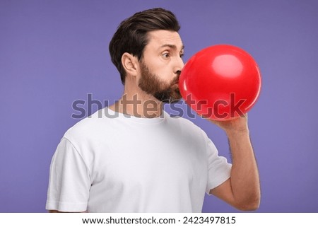 Man inflating red balloon on purple background