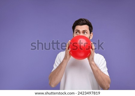Man inflating red balloon on purple background. Space for text