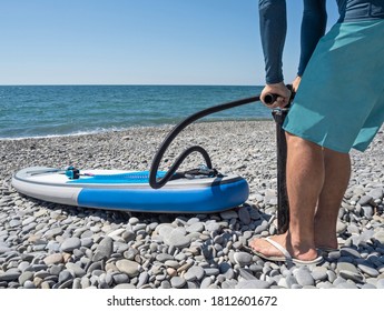 Man Inflating Stand Up Paddle Board With Manual Pump At Sea Background