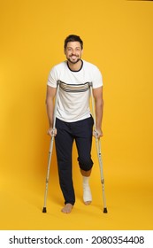 Man with injured leg using crutches on yellow background